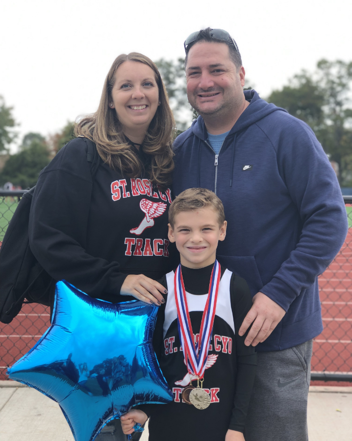 Family standing outside of a track meet, the child has a medal and a balloon